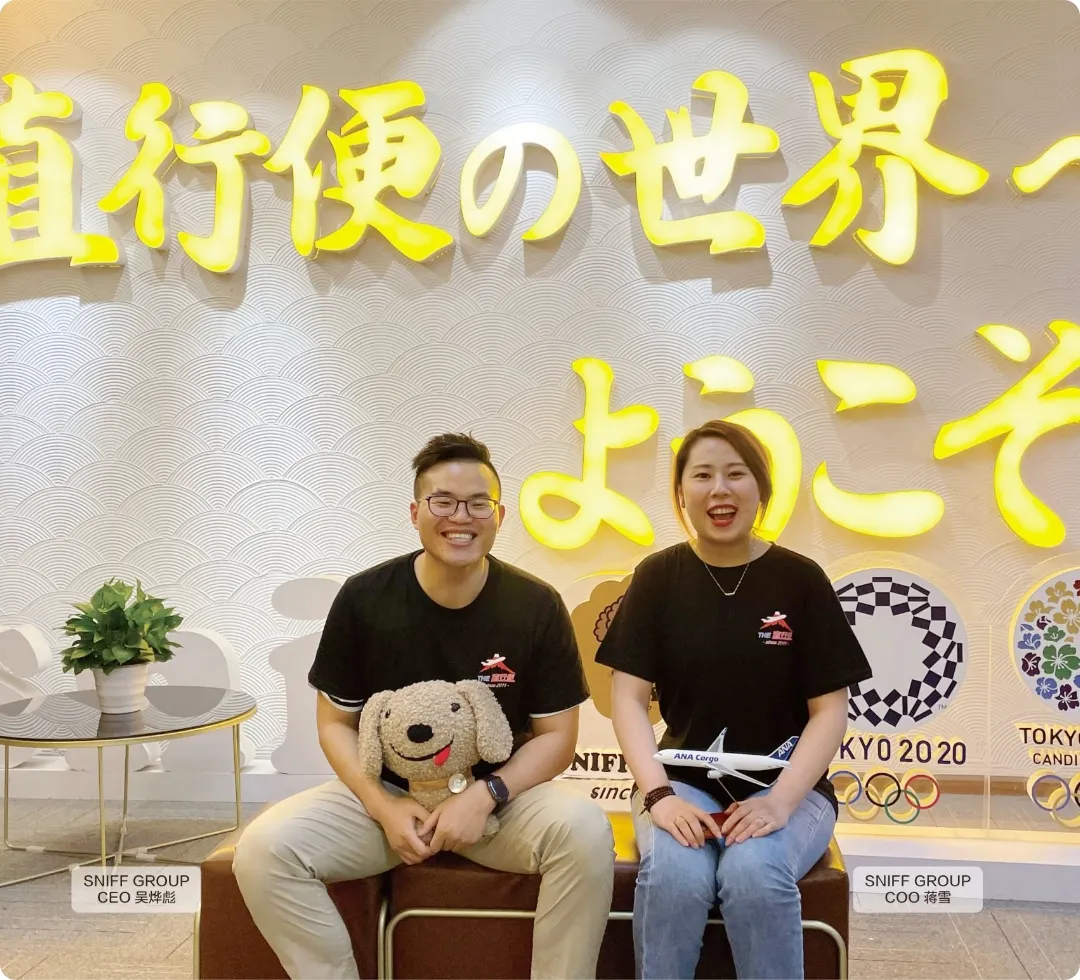 SNIFF GROUP CEO・COOが直行便の世界へようこそと書かれた壁の前で笑顔で座っている