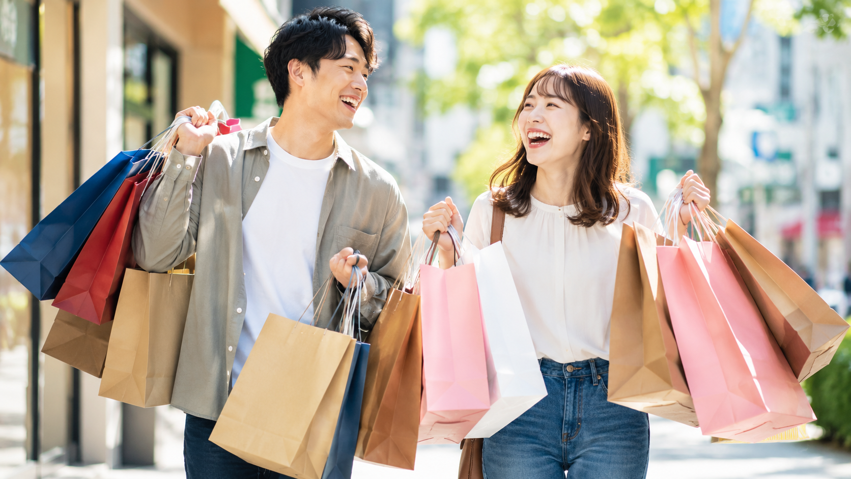 買い物袋を手にいっぱい持って歩く男女　