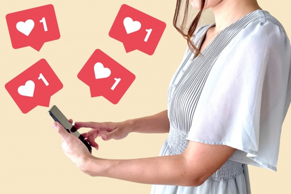 女性が持つスマホといいねマークのイメージ画像